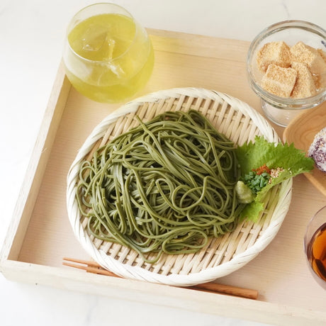 matcha soba noodles served in a round woven plate on a light wooden tray by yunomi.life